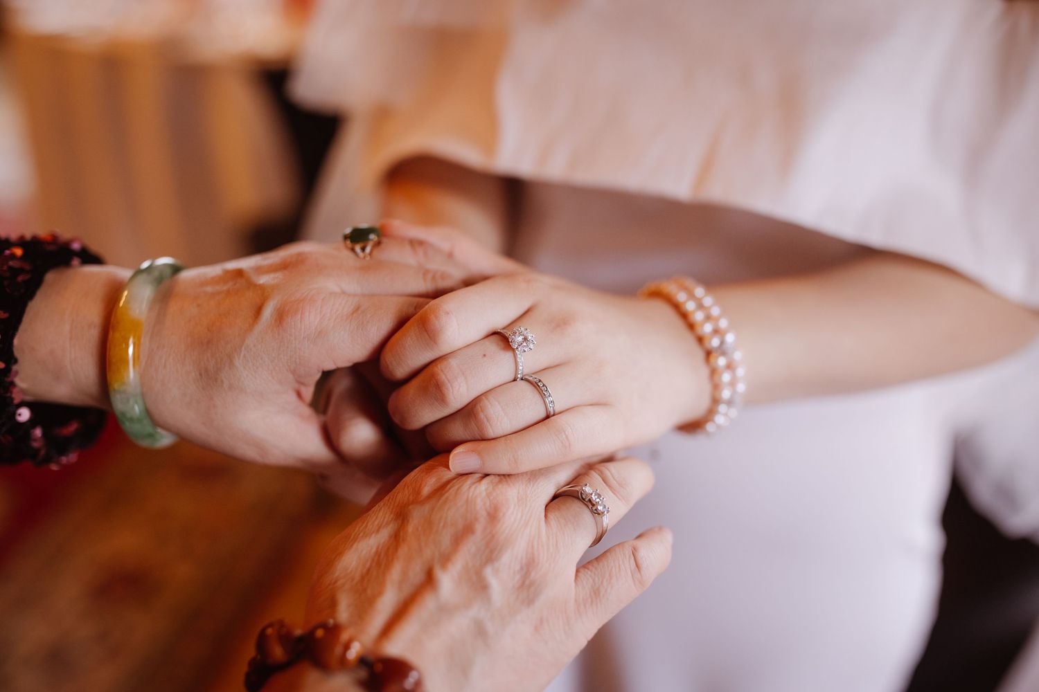 Close-up shot of hands wearing wedding rings and jewelry with romantic lighting.