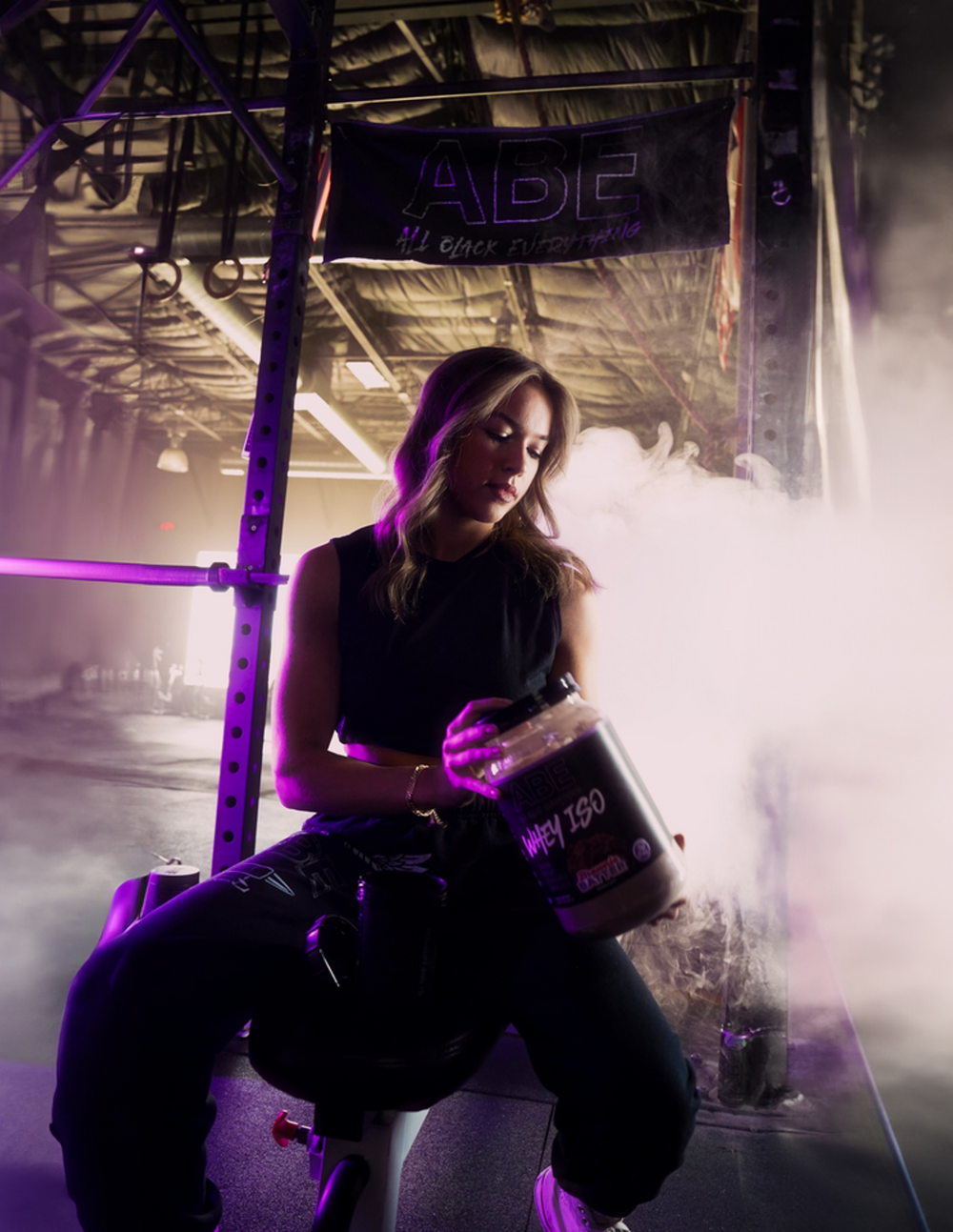 ABE athlete promoting WHEY ISO protein supplement in dramatic gym setting with neon lighting and fitness branding.
