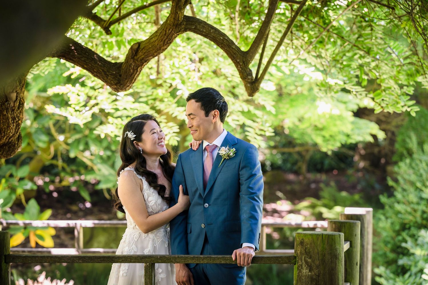 An intimate wedding portrait captured under twisted tree branches in a garden setting.