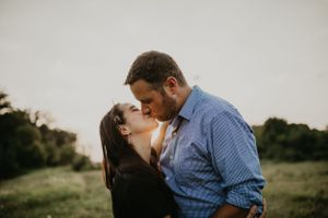 A couple embraces in a tender moment against a light background during sunset.