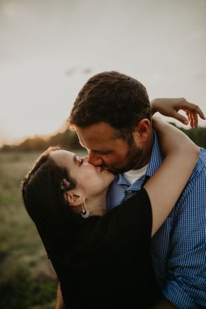 A romantic couple shares an intimate kiss outdoors during golden hour.