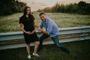 A couple shares playful moments sitting on a metal guardrail at sunset.