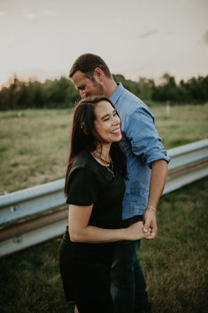 A couple laughs and embraces near a guardrail during an outdoor photo session.