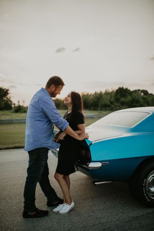 A couple poses intimately against a classic blue car during a sunset photoshoot.