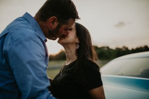 A romantic moment captured between a couple beside a vintage blue automobile.