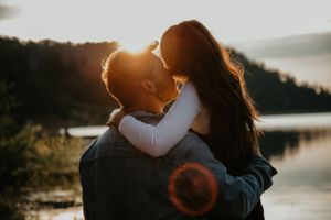 Silhouetted couple shares tender moment at sunset by a mountain lake.