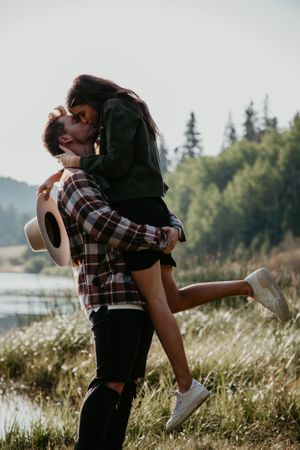 Playful couple dances and embraces in field of tall grass by lakeside.