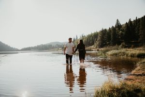 Couple wades together in peaceful lake waters during sunset photoshoot.
