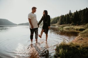 Couple walks hand in hand through shallow water at scenic lakeside location.