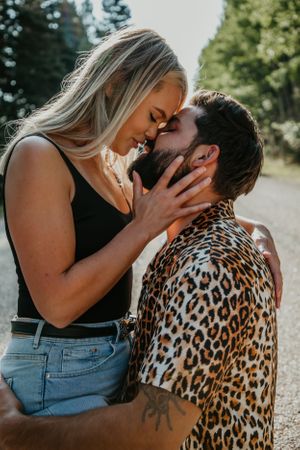 Couple shares passionate kiss during outdoor summer photoshoot on gravel path.