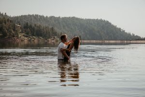 A couple embracing in a serene lake with mountains and forest in the background.