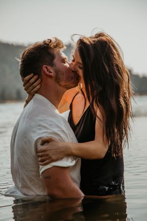 A couple sharing tender moments while standing in lake water at sunset.