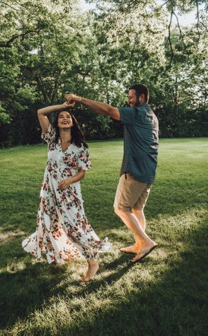 Couple dancing and twirling playfully on grass in golden afternoon light.