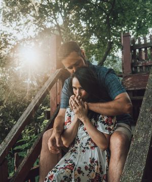 Couple sharing tender moments while sitting on wooden steps in dappled sunlight.