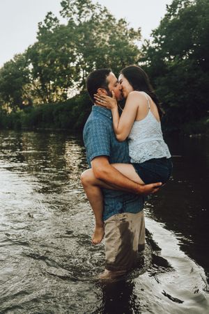 Couple embracing while standing in shallow water during sunset.