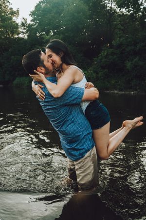 Romantic couple playing and embracing in water during outdoor photoshoot.