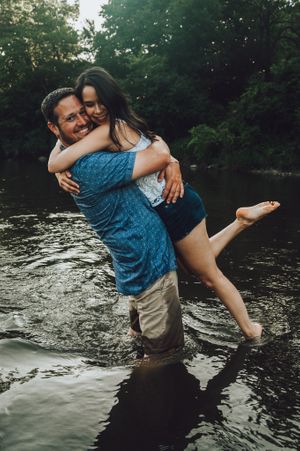 Playful couple splashing and embracing in a lake during a sunset photoshoot.