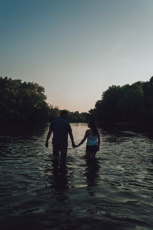 Silhouettes of people wading in a tranquil lake at sunset with trees lining the shore.