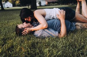 Couple lying together in grass during golden hour outdoor photoshoot.
