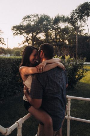 Romantic couple embracing on a white railing at sunset in an outdoor setting.
