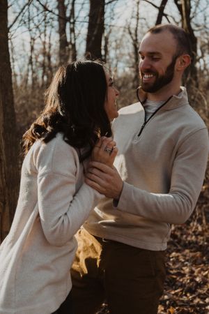 A couple in matching white sweaters shares playful moments in an autumn forest.