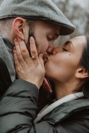 Couple sharing passionate kisses while wearing winter clothing outdoors.