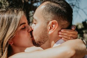 A couple shares a passionate kiss during an outdoor photo session in natural lighting.