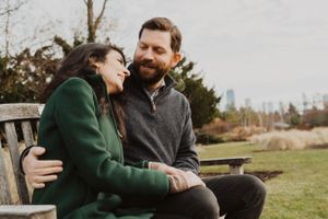 Couple sharing tender moment on bench during outdoor autumn photoshoot.