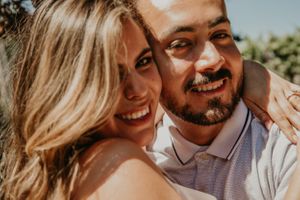 A couple shares a loving moment while smiling in warm sunlight outdoors.