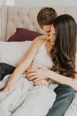 Couple cuddling together on comfortable bed with textured white blanket.