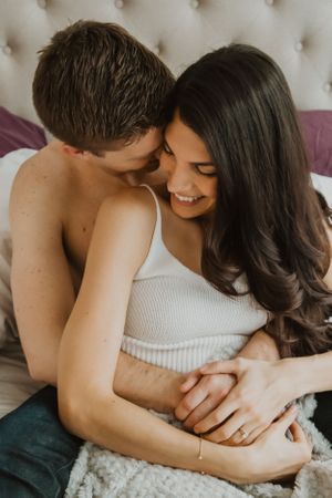 Romantic couple embracing while relaxing together on tufted headboard bed.