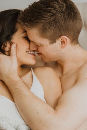 Tender moment between couple lying close together in soft lighting.