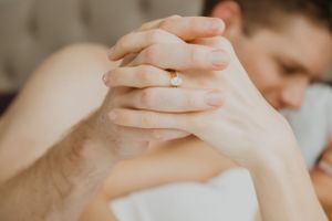 Couple embracing intimately on white bedding in natural morning light.