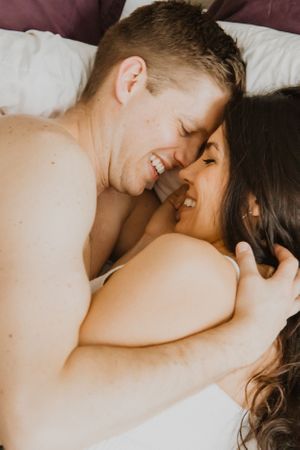 Intimate couple sharing tender moments while lying together in bed with white sheets.