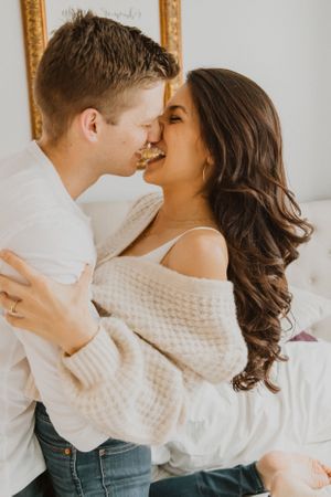 A couple in white sweaters shares intimate moments in an indoor photoshoot.