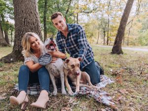 Happy couple sitting on grass with their dogs during an autumn engagement session.