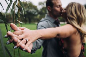 Close-up shot of hands displaying an engagement ring in an outdoor setting.