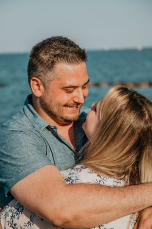 A couple embraces tenderly by the ocean during a sunny beach photoshoot.