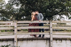 Couple sitting together on a rustic wooden fence in a serene country setting.
