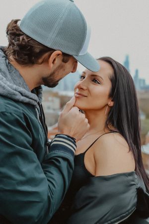 Intimate close-up of a couple in casual attire with baseball caps against an urban backdrop.