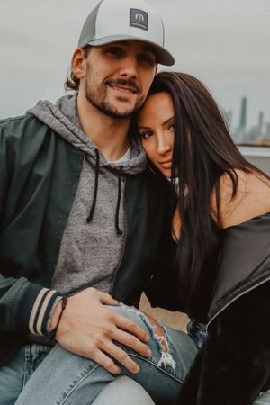 Casual couple in baseball caps and hoodies sharing a tender moment outdoors.