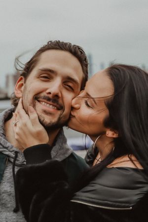 Playful couple sharing affectionate kisses and laughter in moody outdoor lighting.