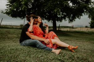 Couple sitting on grass under trees during a romantic outdoor photoshoot.