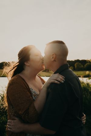 A tender moment between a couple kissing in a sunlit field at sunset.