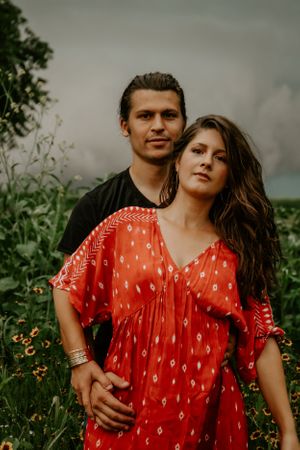 A couple embraces outdoors wearing red and black clothing against a natural background.