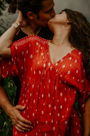 An intimate moment captured between a couple with one wearing a vibrant red patterned dress.