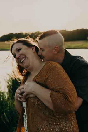 A joyful couple laughs and embraces during a romantic outdoor photoshoot at golden hour.