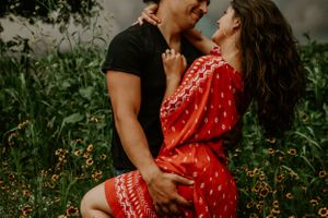 Intimate couple's photoshoot in a field with wildflowers and moody lighting.