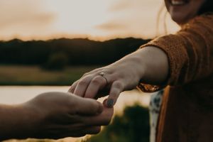 Silhouetted hands reaching towards each other against sunset sky.