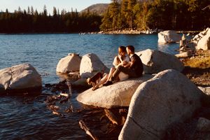 People relaxing on large rocks by a scenic mountain lake during sunset.